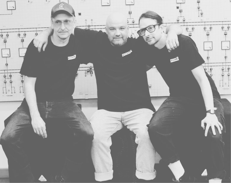 Les trois membres de room8 assis côte à côte, photo de groupe en noir et blanc